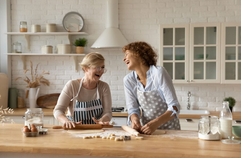 An older adult woman and her daughter, smiling and baking together in the kitchen.