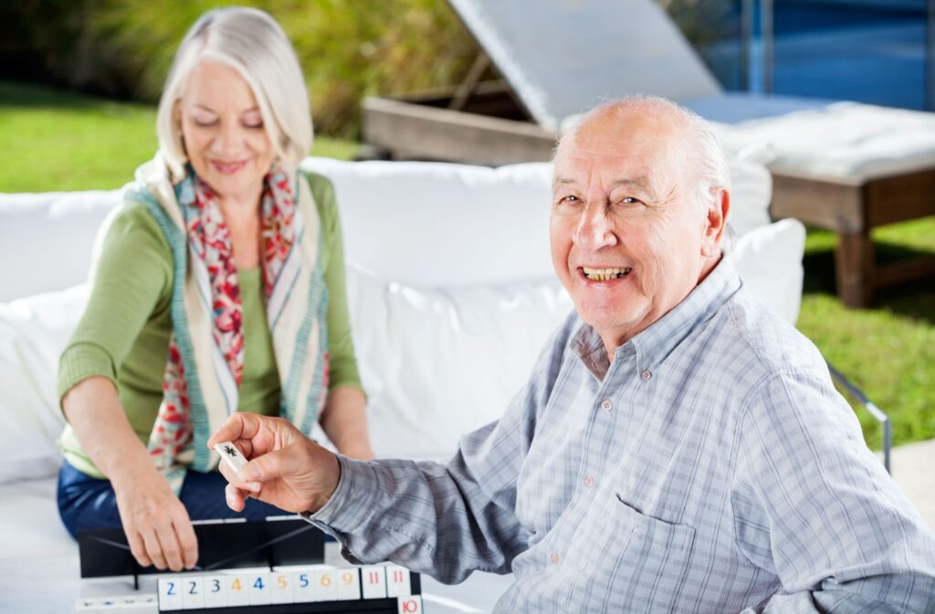 A senior man and woman smiling and playing Rummikub.