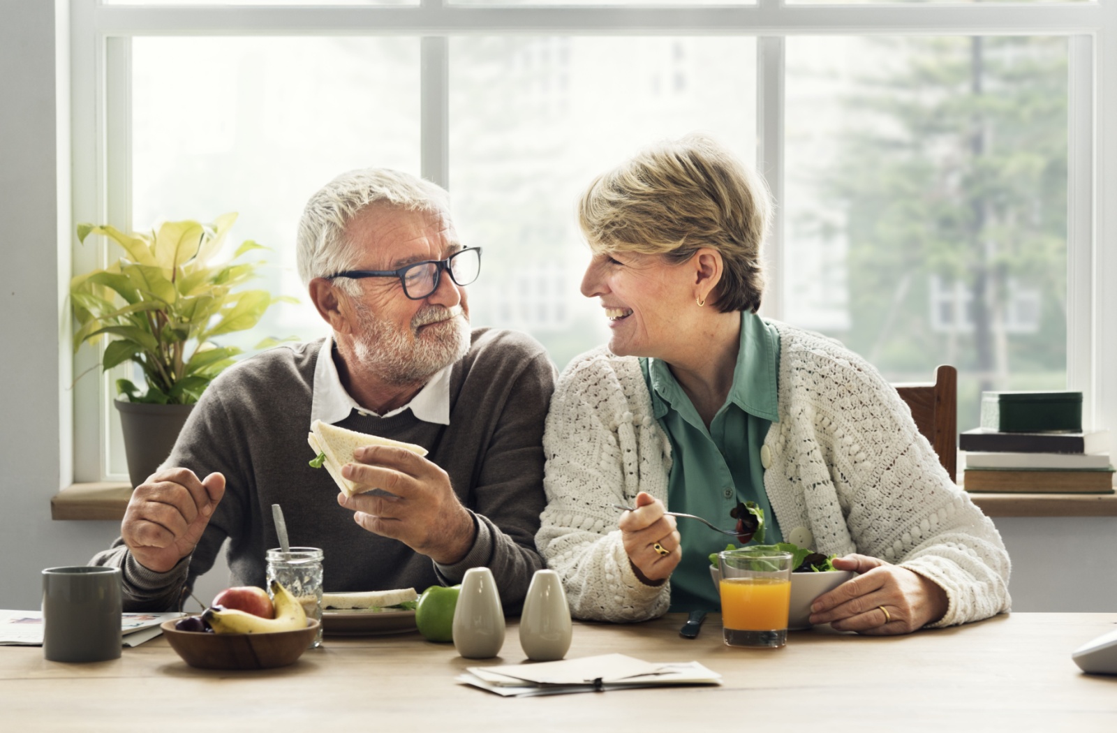 An older adult couple smiling at each other as they enjoy a meal together.