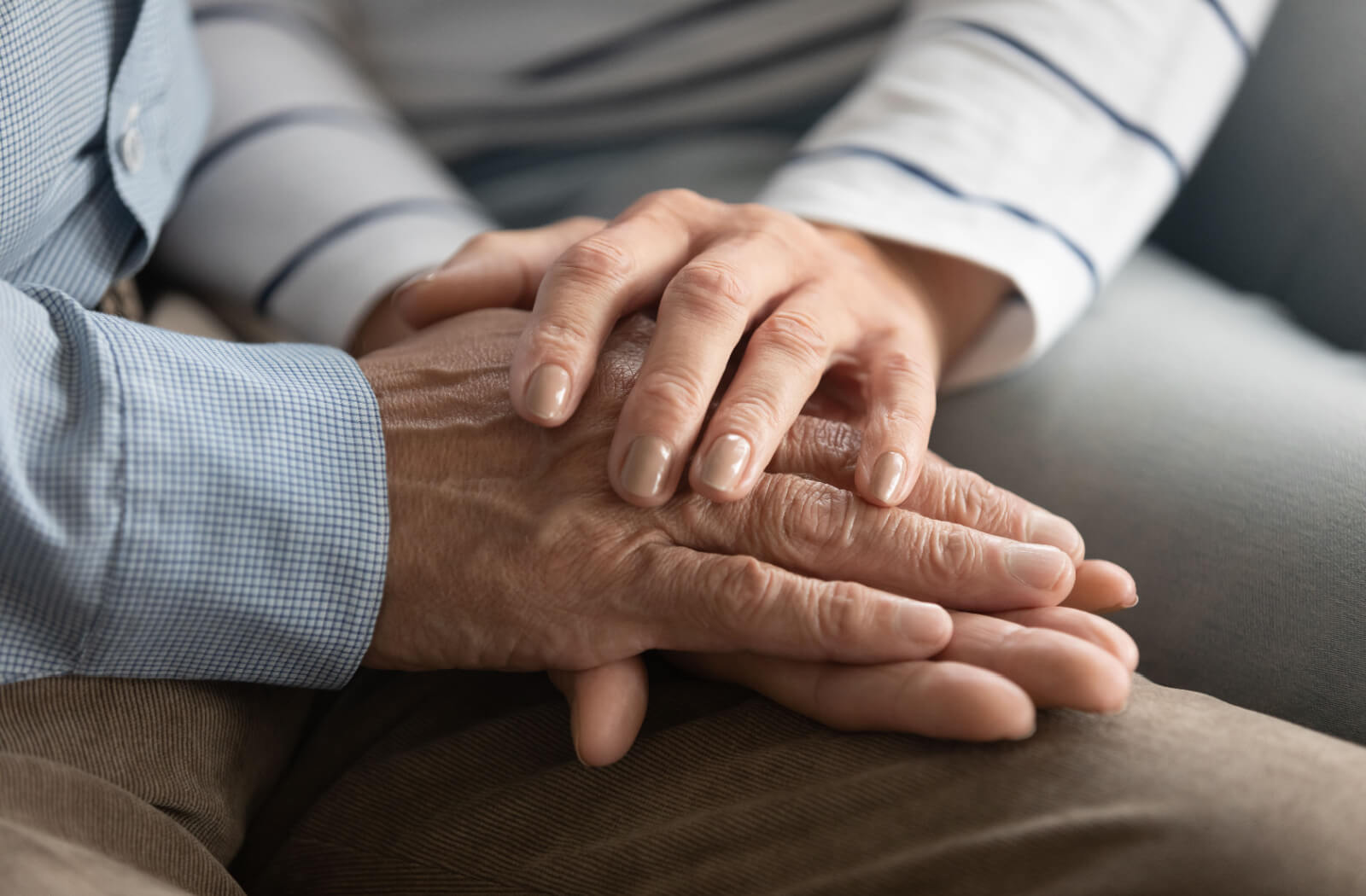 A close-up of an adult and their parent's hands, offering reassurance and coping with the decision to move to assisted living.